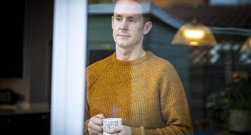 Rob, who lives with CML, stands looking out of a window, holding a mug.