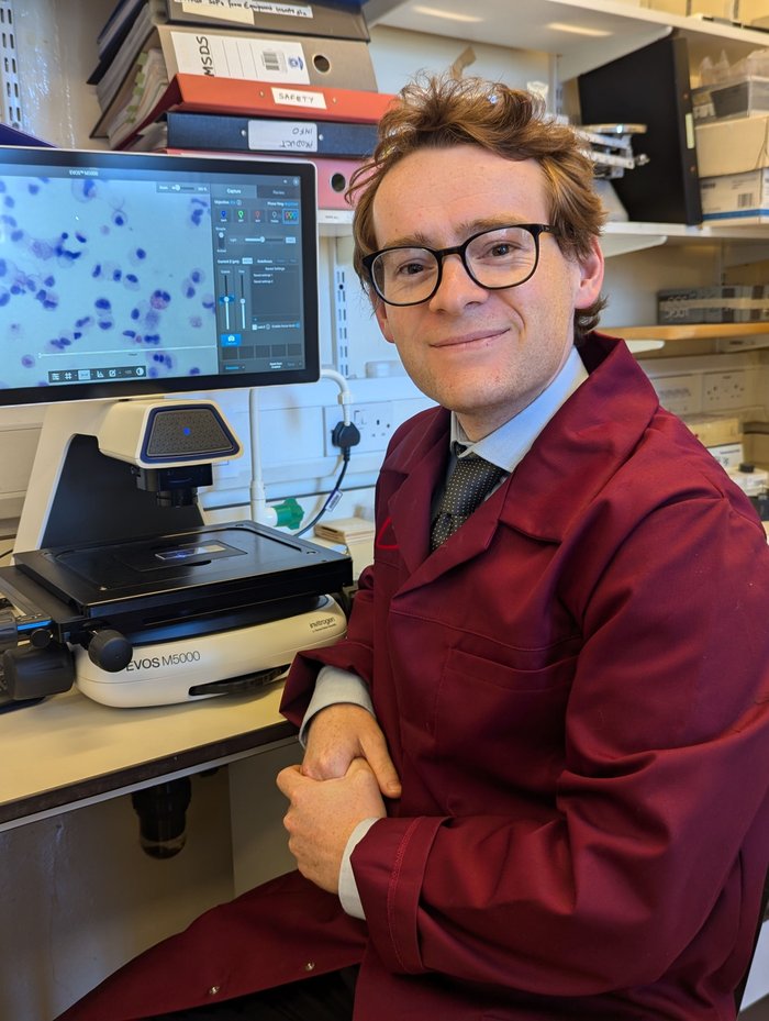 Dr Aidan Haslam, sat in research lab next to his computer