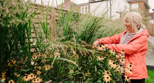 An older woman smiles as she works in her garden.