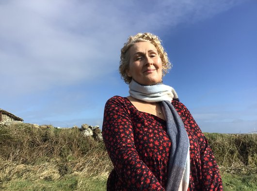 Rebecca stands smiling outside in the sunshine with a blue sky in the background.