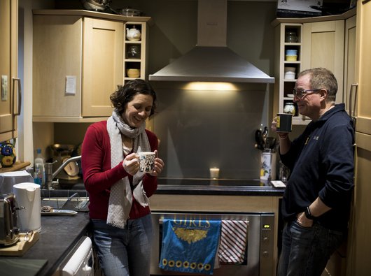 Paul, living with CML, has a cup of tea with his wife laughing wife in the kitchen.