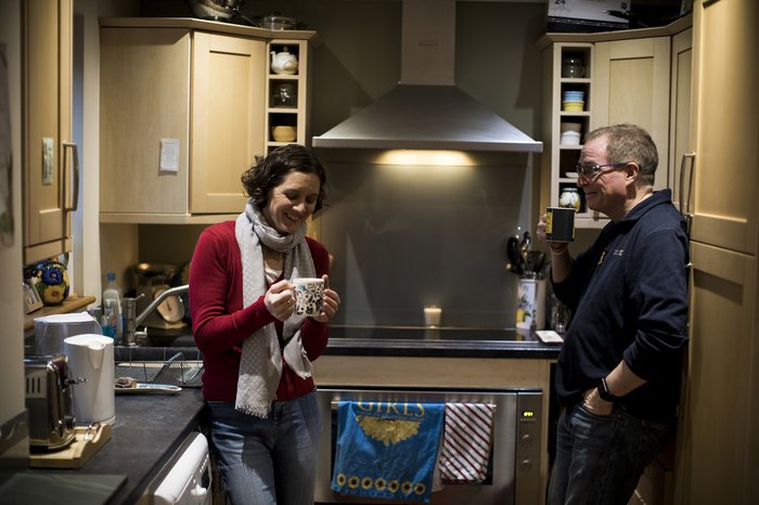 Paul, living with CML, has a cup of tea with his wife laughing wife in the kitchen.