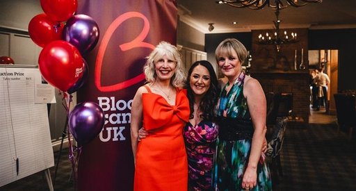 A group of women at a Let's Beat It Blood Cancer UK event, standing in smart clothing next to banners and balloons.