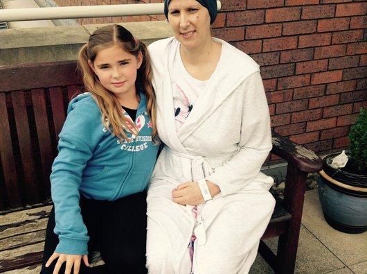 Two women sat on a wall. One going through cancer treatment.