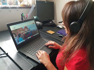 A Blood Cancer UK support line worker working at her laptop with headphones on, surrounded by office equipment.