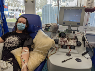 Ben sits in a hospital chair donating stem cells via a catheter in his arm.