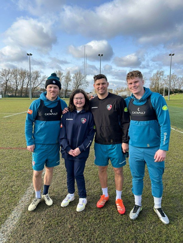 Poeple smiling on a rugby pitch in a line