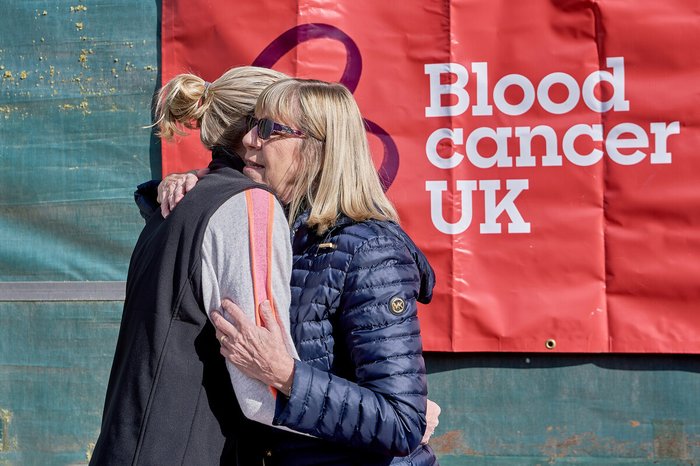 Two people hugging in front of a Blood Cancer UK flag
