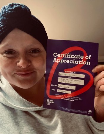 Image of Bracken Baines wearing headscarf, hoody and holding a Blood Cancer UK fundraising certificate