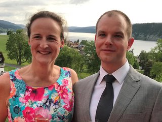 A woman - Carina - poses with a male friend at a formal function in the countryside on an overcast day.