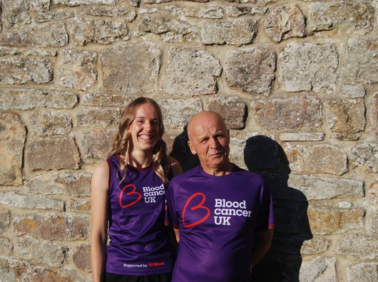 Charlotte and her father stand against a wall in Blood Cancer UK running gear.