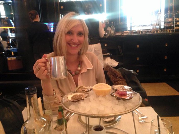 Charlotte as a adult, smiling as she eats oysters in a restaurant