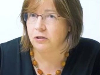 A headshot of Professor Claire Harrison, wearing glasses and talking.