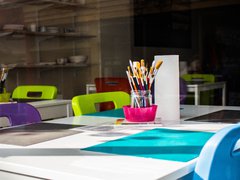 A stock image of a school desk with blue writing mats and purple and green chairs tucked into the table.