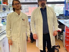 Professor Claus Nerlov stood in the lab smiling alongside his post-doc student, both are wearing lab coats.