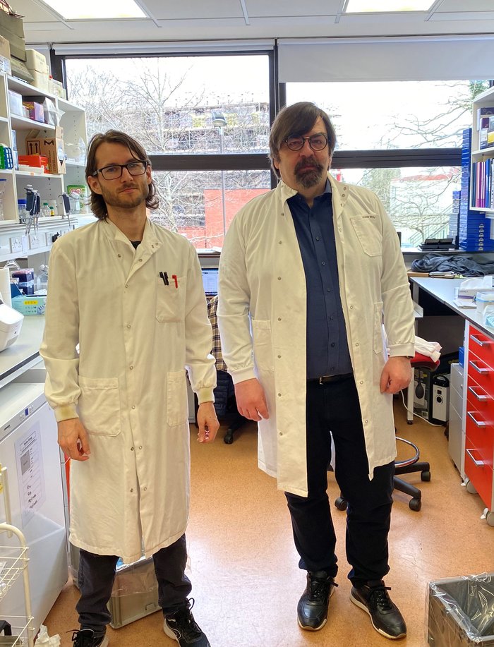 Professor Claus Nerlov stood in the lab smiling alongside his post-doc student, both are wearing lab coats.