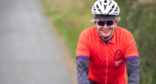 A cyclist heading down a country lane wearing a red Blood Cancer UK T shirt.