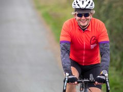 A cyclist heading down a country lane wearing a red Blood Cancer UK T shirt.