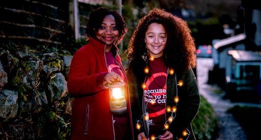 Two people smiling and holding lanterns under a moon-lit sky at a Walk of Light event.