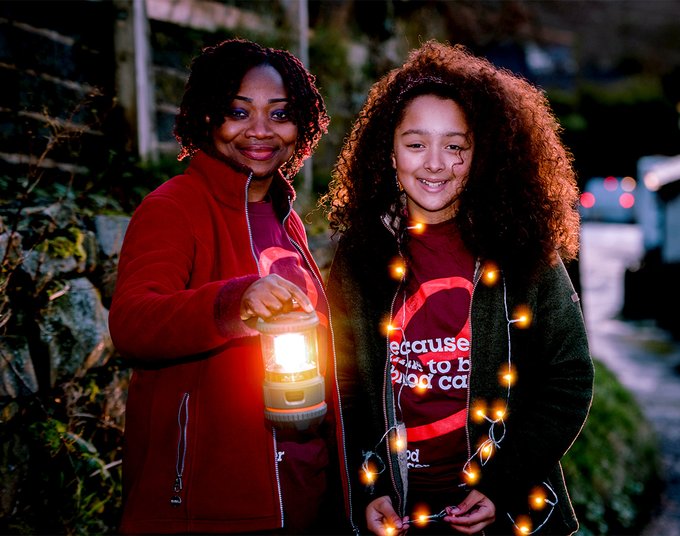 Two people smiling and holding lanterns under a moon-lit sky at a Walk of Light event.