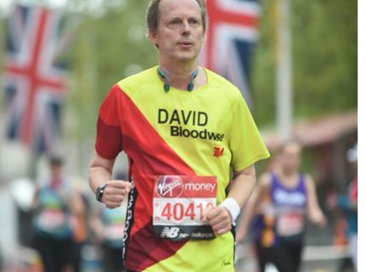 An older middle-aged man - David - runs a marathon wearing a Bloodwise jersey.