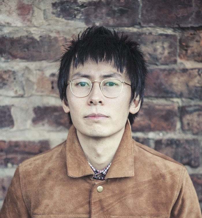 Head and shoulders shot of David, standing against a brick wall.