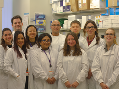 Dr Claire Roddie and her nine team members stood together in the lab, wearing lab coats, facing the camera smiling.