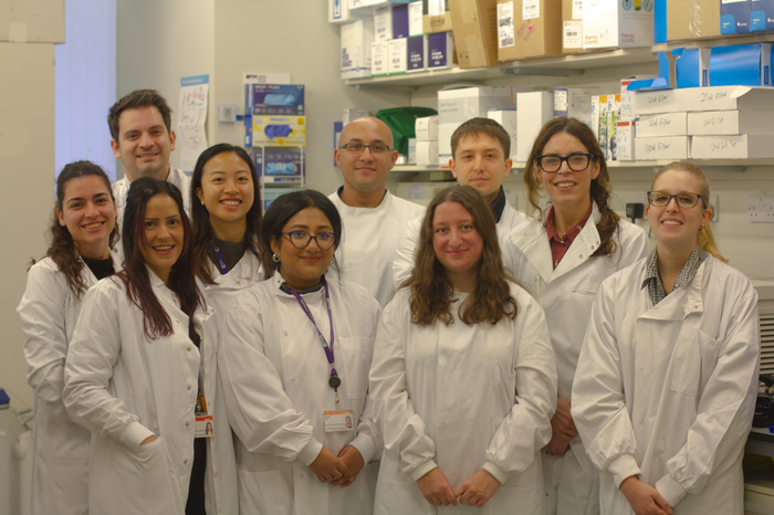 Dr Claire Roddie and her nine team members stood together in the lab, wearing lab coats, facing the camera smiling.