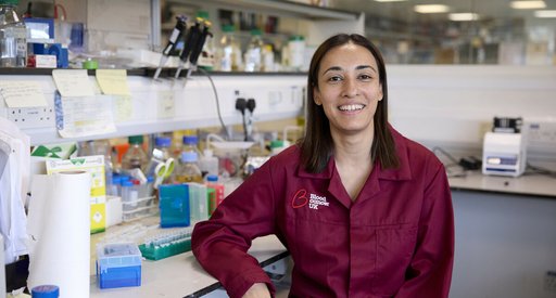 Dr Jasmeen Oberoi stood smiling in the lab wearing a Blood Cancer UK lab coat.