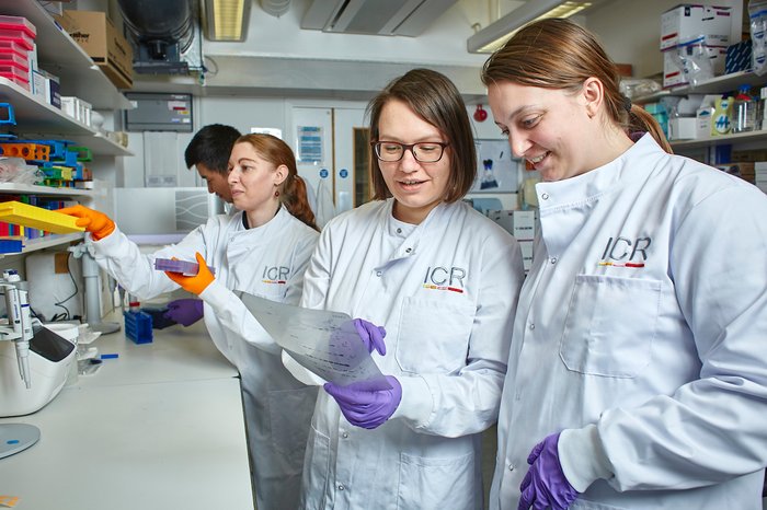 A lady working in the lab with other members of the lab team, all wearing white lab coats.