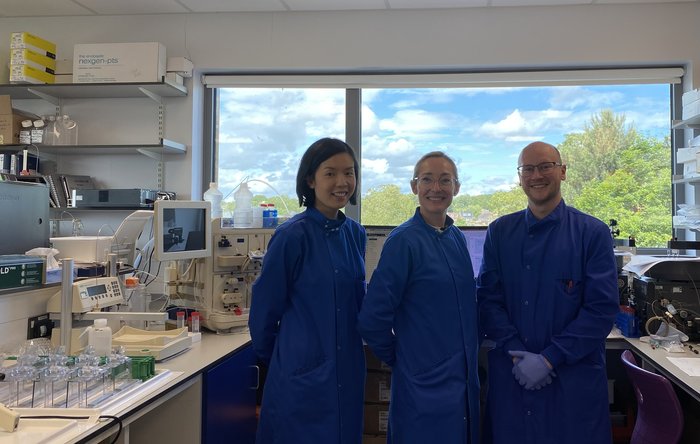 Dr Sean Lim and two other lab team members stood together in the lab wearing blue lab coats.