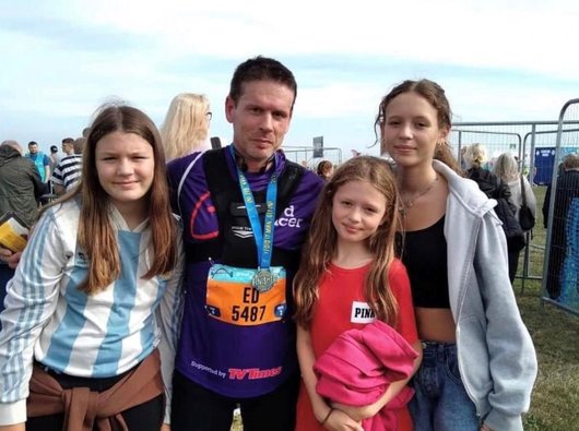 Ed, dressed in a Blood Cancer UK running shirt with a medal round his neck, flanked by his three daughters