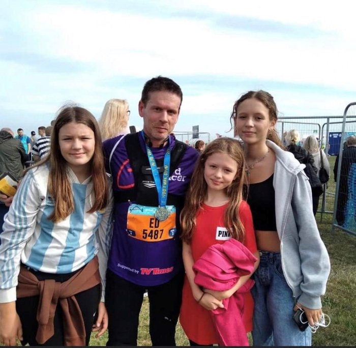 Ed, dressed in a Blood Cancer UK running shirt with a medal round his neck, flanked by his three daughters