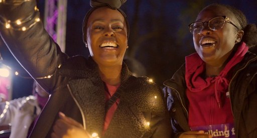 Nadine and friend close up laughing to the camera and holding lights at Walk of Light Birmingham 2024