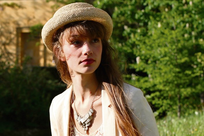 A young woman - Emma - wearing a small straw hat in a garden outside.