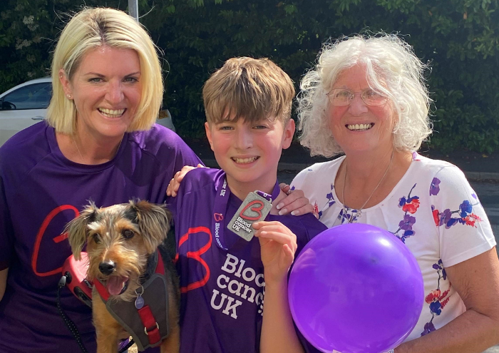 A young boy poses with a Blood Cancer UK medal, flanked by his mother and grandmother.