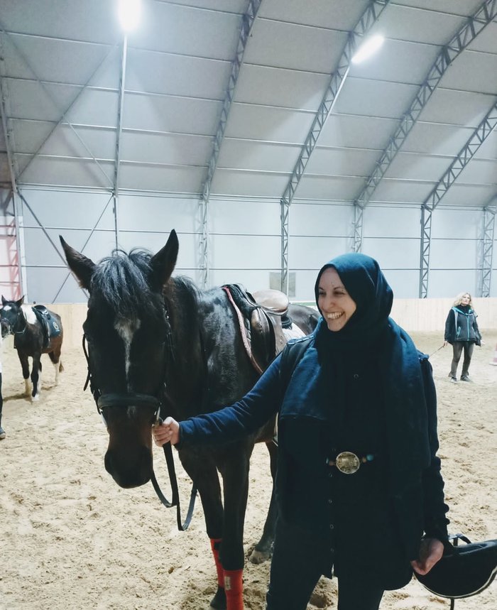 A woman (Federica) smiling in the direction of a horse, which she is stood next to.