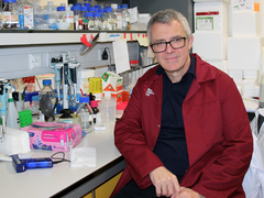 Professor George Vassiliou sat in the lab smiling wearing his lab coat.