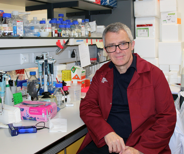 Professor George Vassiliou sat in the lab smiling wearing his lab coat.