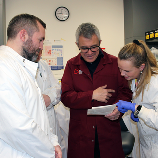 Man in red lab coat working with a women and man in white lab coats