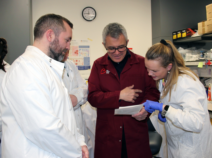 Man in red lab coat working with a women and man in white lab coats