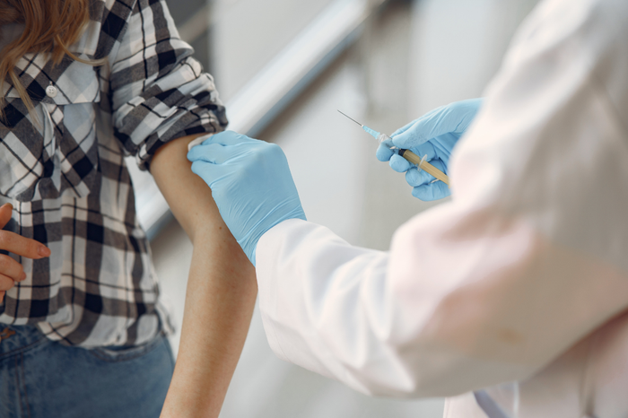 Close up of a doctor with blue gloves who has just injected a blood cancer patient in a checked shirt in their upper arm.