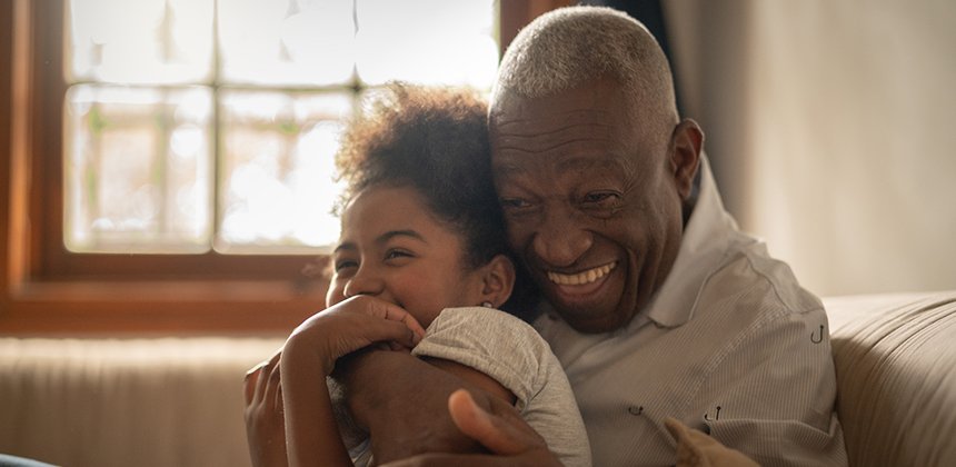 Adult male smiling whilst holding happy daughter.