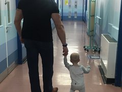 A very young child walks through a hospital corridor with her father.