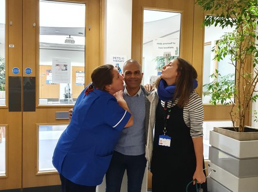 Sunny, who has blood cancer smiling, in a hospital with two nurses leaning on him from either side.