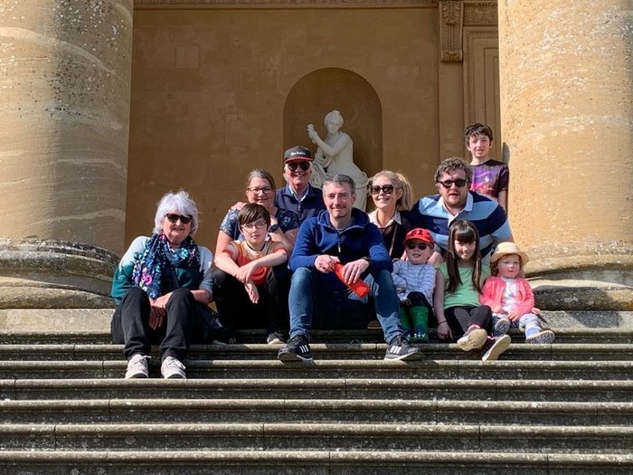Jacqui with all her family around her, seated on some steps at a stately home.