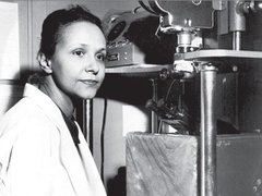 A scientist  - Jane C Wright, surgeon and early chemo researcher, poses next to a microscope in a black and white photograph.