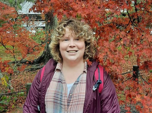 Katherine on holiday in Japan, smiling in front of a colourful maple tree.