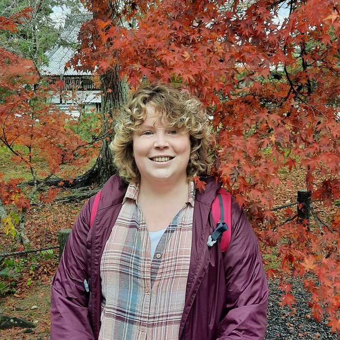 Katherine on holiday in Japan, smiling in front of a colourful maple tree.