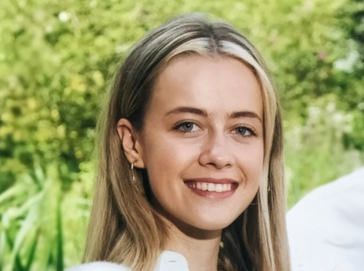 Jasmine Handford, trustee of Blood Cancer UK, smiling at the camera in front of foliage backdrop.